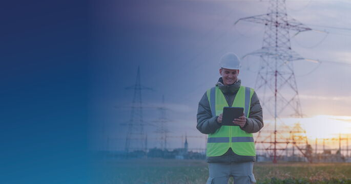 Mitarbeiter eines Energieversorgers mit Tablet vor Strommasten und Hochspannungsleitungen.