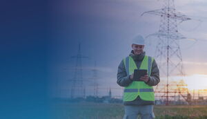 Mitarbeiter eines Energieversorgers mit Tablet vor Strommasten und Hochspannungsleitungen.